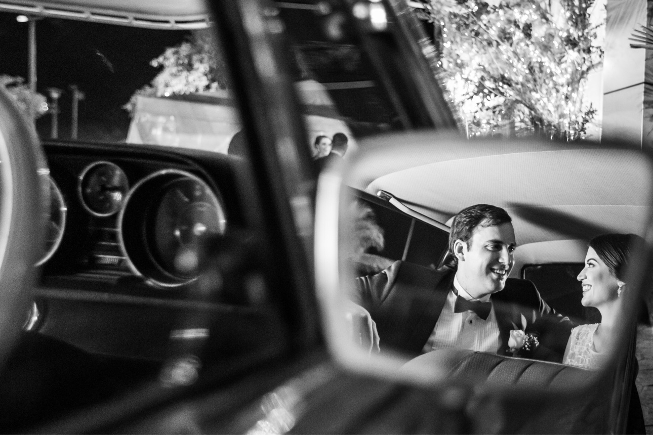 Newlyweds smiling at one another in the reflection of a classic car mirror