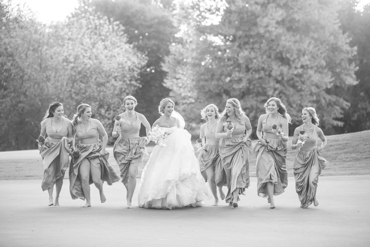 Bride and bridesmaids running together outdoors in a joyful black-and-white photograph