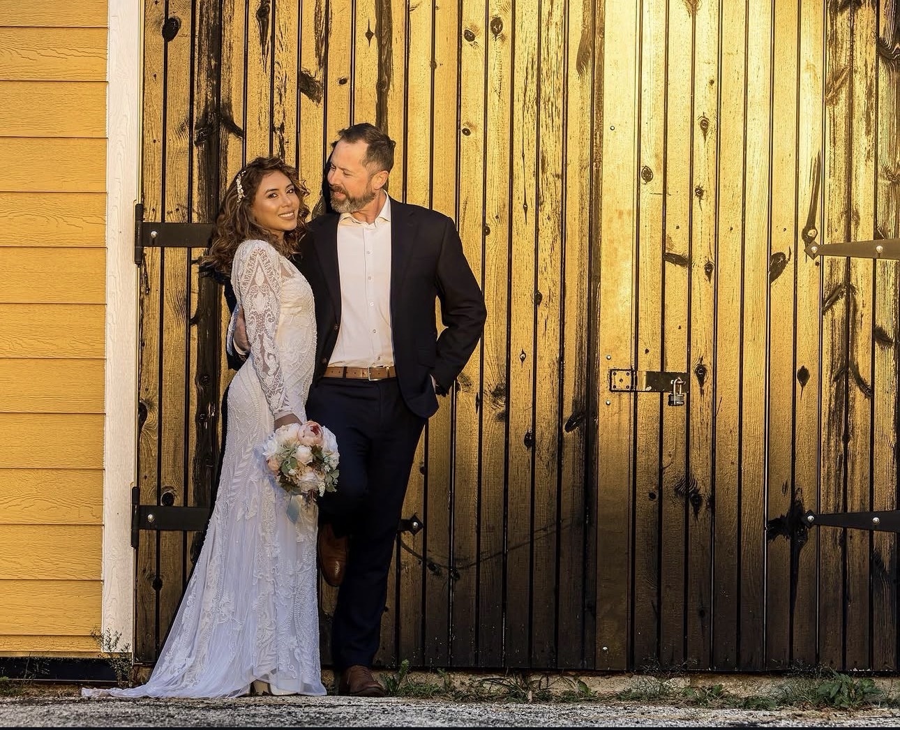 Newlyweds standing together before a grand golden barn door