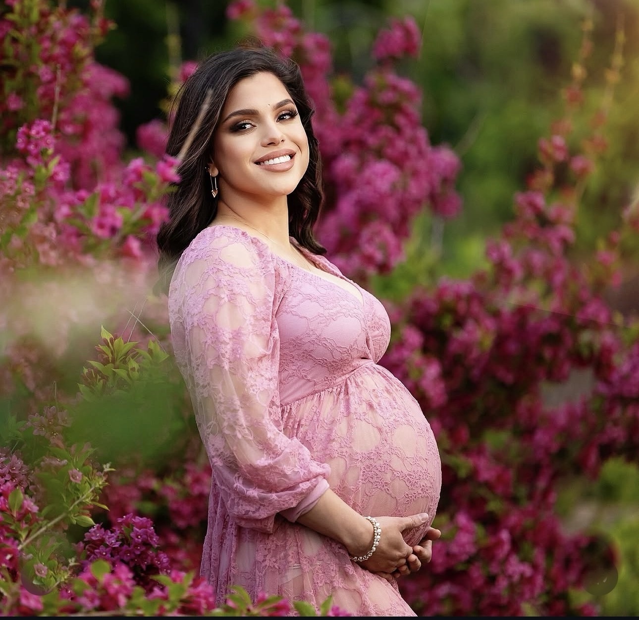 Expectant mother in a rose lace dress surrounded by vivid pink flowers